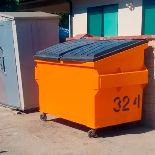 A professional commercial front-load dumpster featuring a bright orange body and heavy-duty black plastic lids. The container is equipped with wheels for easy maneuvering and is positioned against a building wall, showcasing reliable commercial waste collection and scheduled trash pickup services for businesses.
